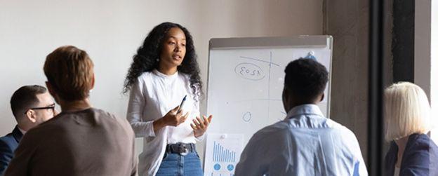 A presenter at a whiteboard speaks to four people